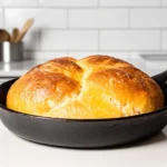 Pan de Maicena dorado en una sartén negra sobre un mostrador de cocina blanco.